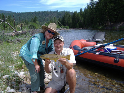 Two guests standing next to a river and a boat show off their recent catch