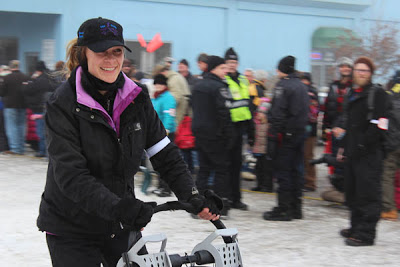 A happy women pushing a sled led by dogs.