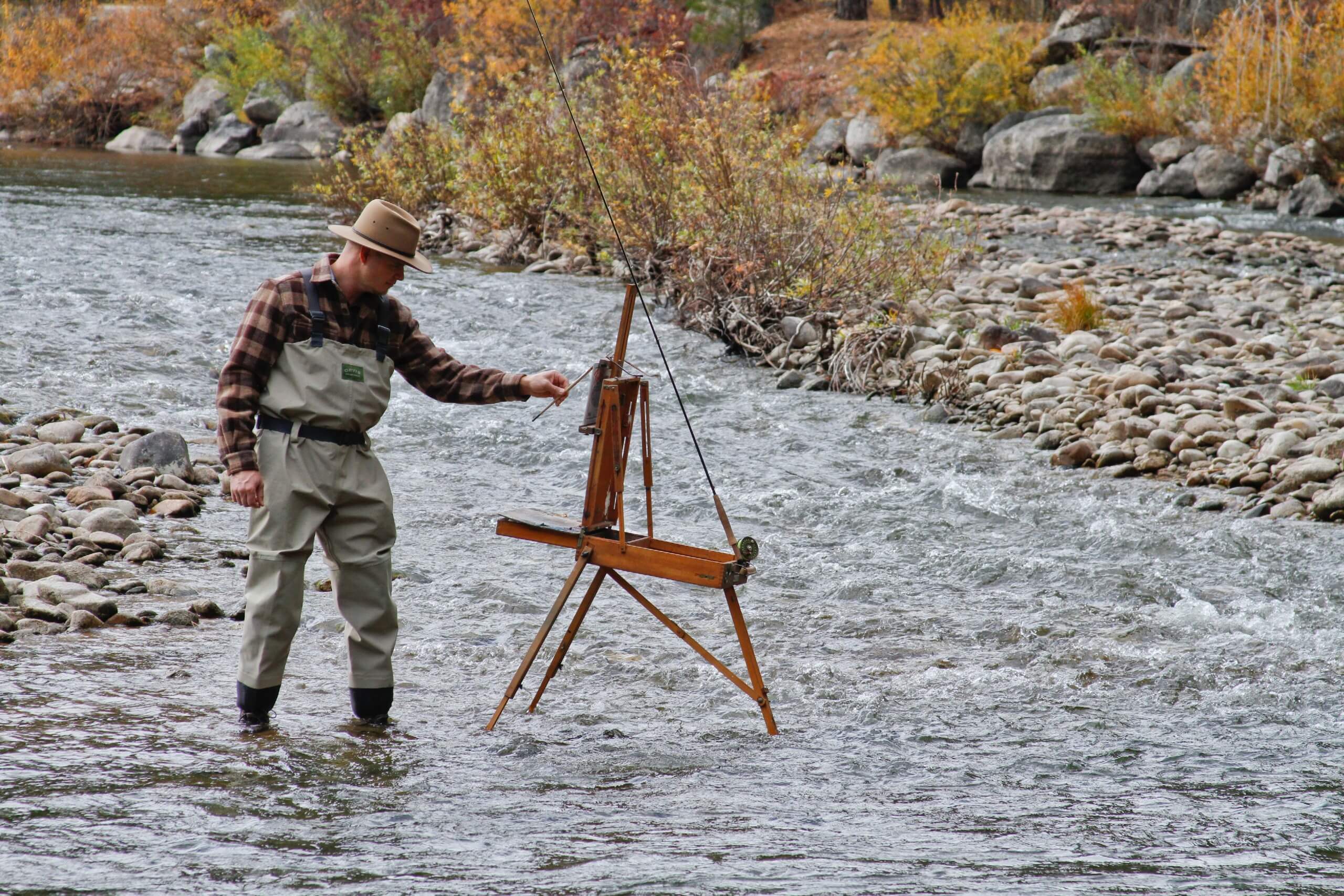 artist painting on an easel set in the river