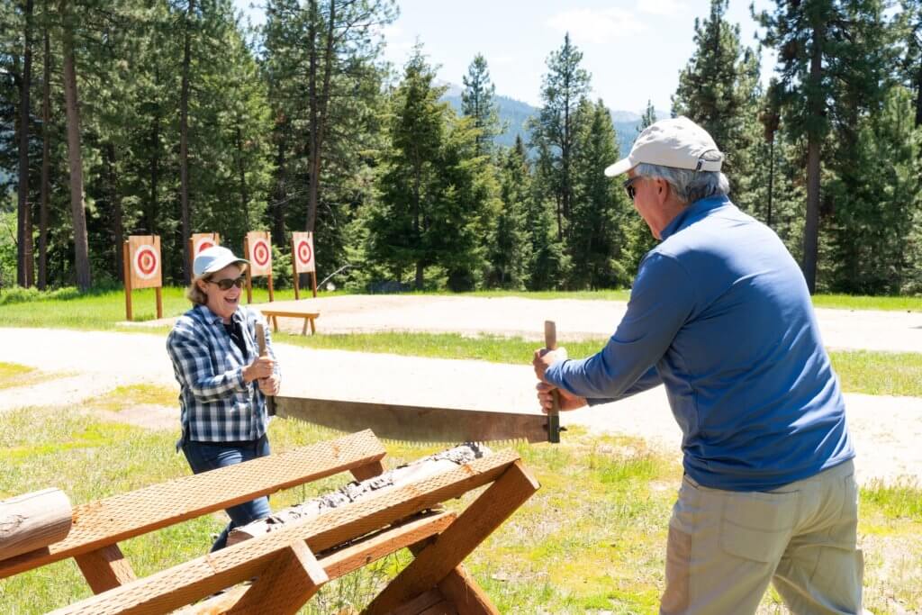 Guests saw a log at logging camp in the mountains.