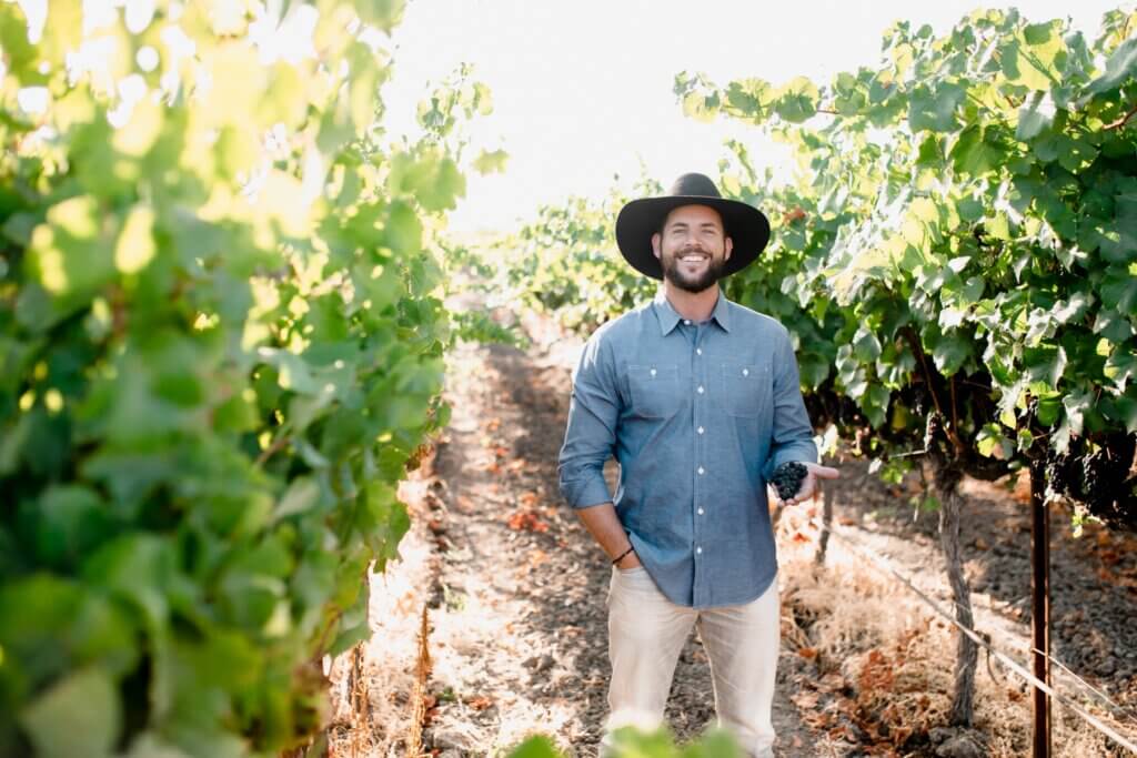 Ryan Hill holding grapes while standing in front of a vineyard