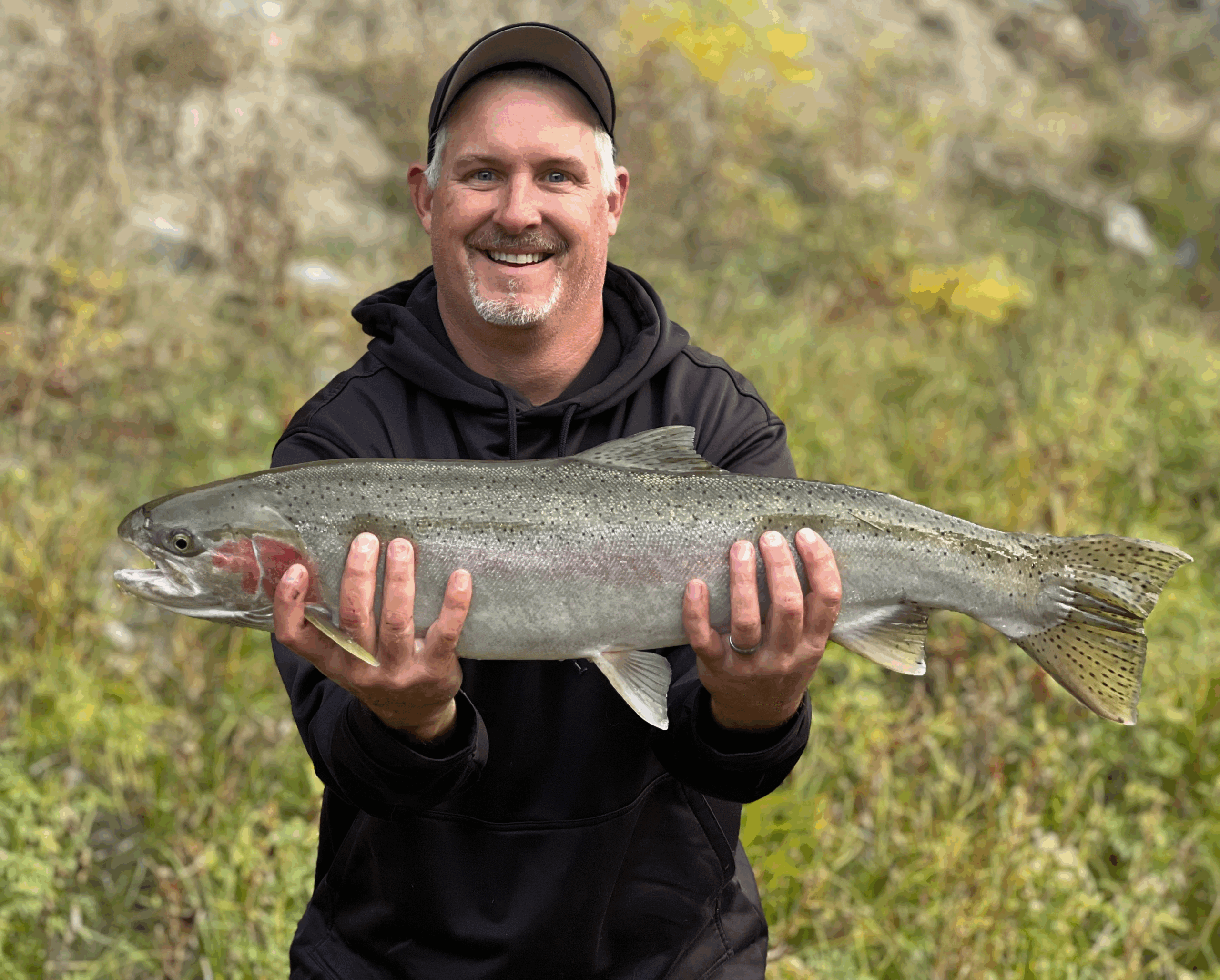 A man in a black baseball hat and jacket holds a massive fish in both hands