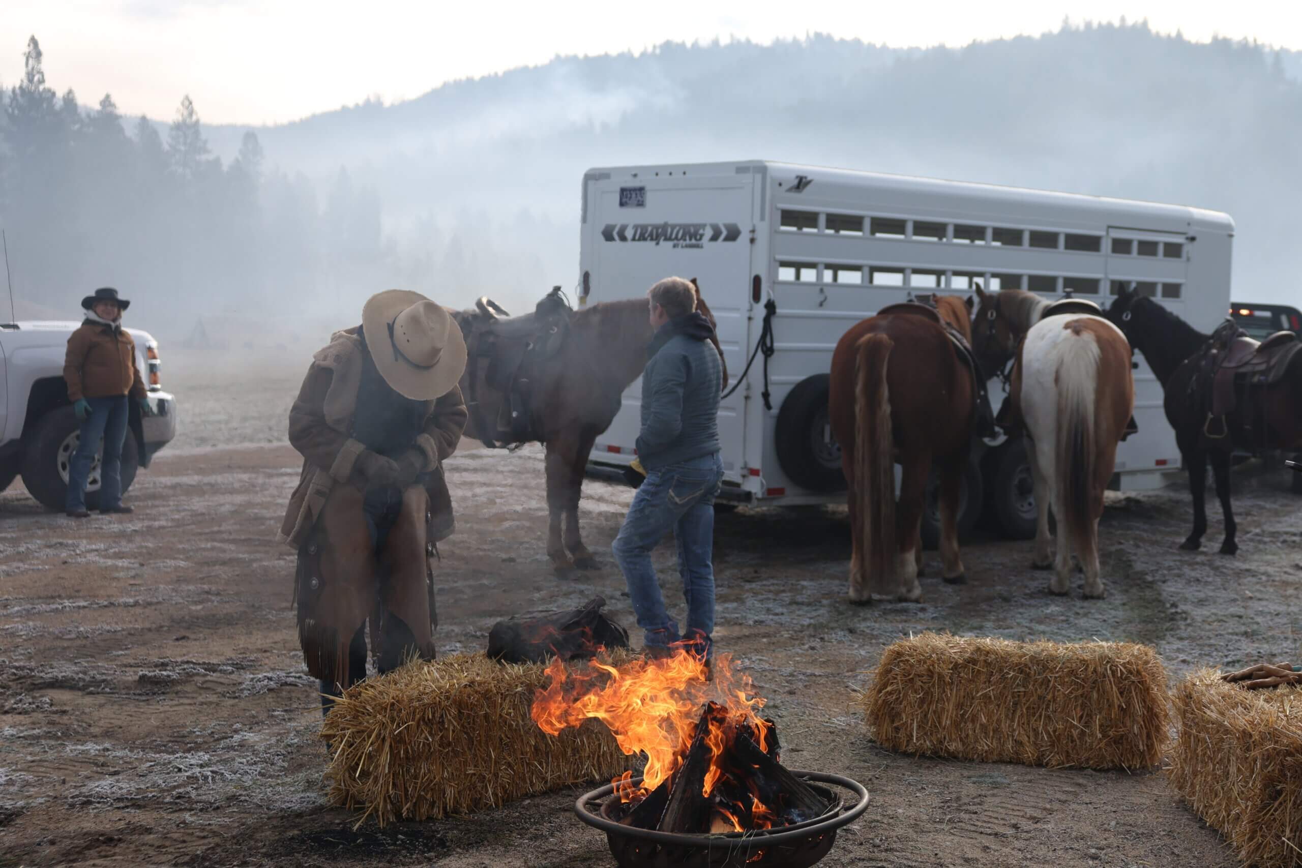 Triple Creek Ranch Guests enjoying campfire by haybales and horse trailer preparing for Roping during Cattle Team Penning activity for the annual Cowboy School Event