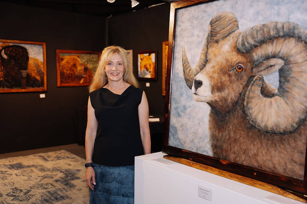 Wool and felt artist Karen Straight standing next to her piece featuring a large male big horn sheep